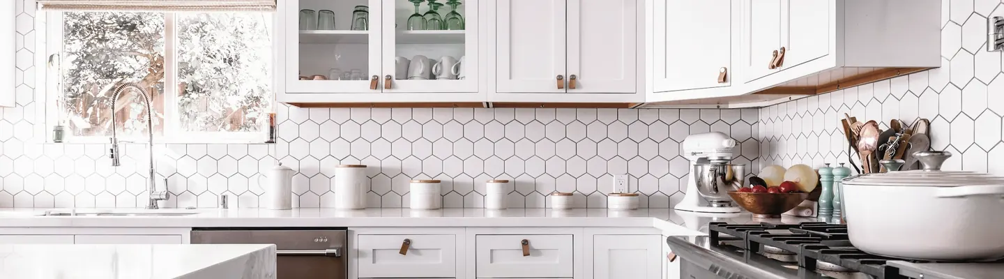 A bright kitchen with white cabinets, hexagonal wall tiles, and a marble island